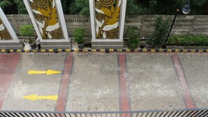 Vista de un estacionamiento con flechas direccionales en el suelo, rodeado por una barandilla metálica y un muro decorativo con motivos de hojas.