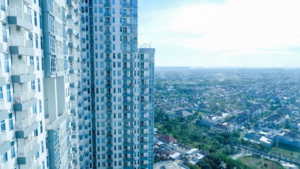 A high-rise building with multiple balconies and a view of a residential area below. - Spacey And Homey 2Br At Supermall Mansion Apartment (Surabaya)