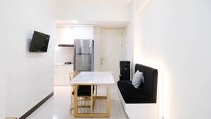 A compact kitchen with a refrigerator, stove, and a TV mounted on the wall. - Spacey And Homey 2Br At Supermall Mansion Apartment (Surabaya)