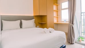 Ett hotellrum med en säng, en garderob i trä, hyllor vid sängen och ett fönster med gardiner.