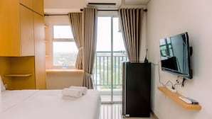 Ett hotellrum med en säng, en platt-TV, ett minikylskåp och ett fönster med gardiner.