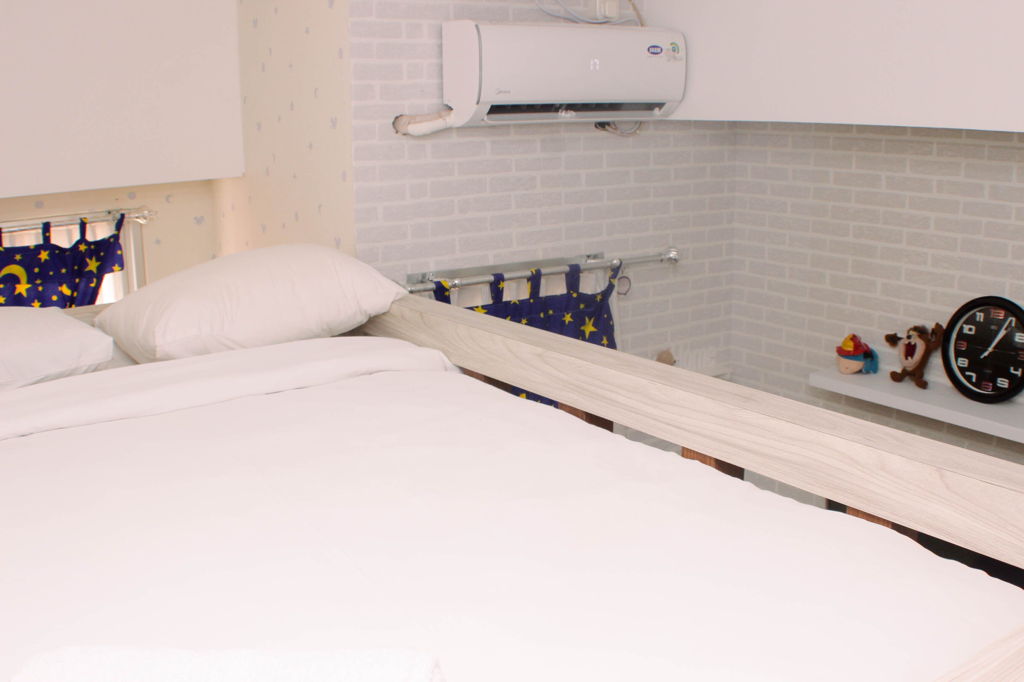 Een slaapkamer met een bed, nachtkastje, klok en een luchtverkoeler aan de muur.