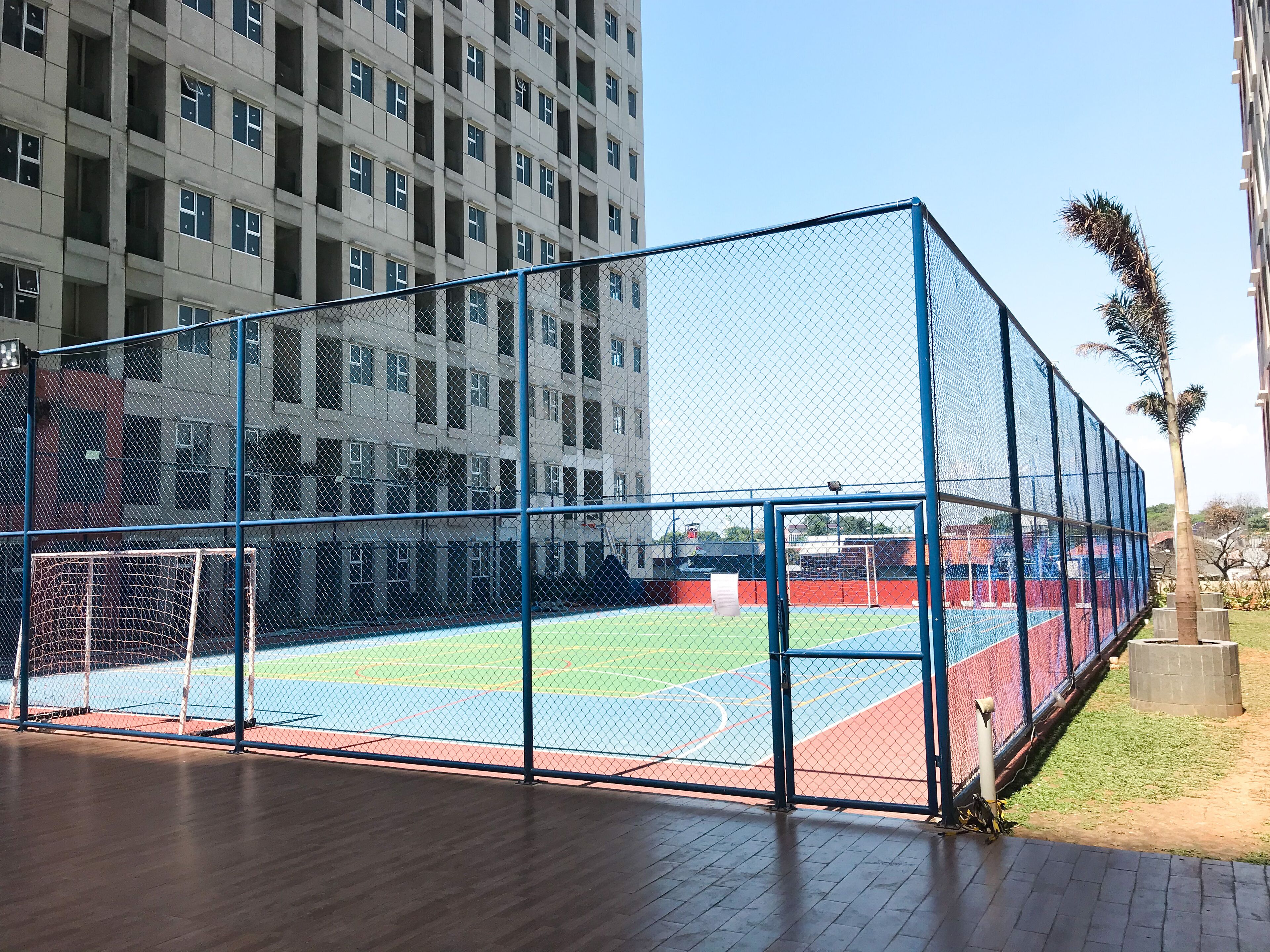 A sports court with a blue fence, surrounded by a building with multiple windows.