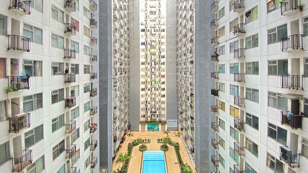 A high-rise residential building with multiple balconies, a central courtyard with a swimming pool, and a view of the surrounding area. - Homey 1Br At Jarrdin Cihampelas Apartment (Bandung)
