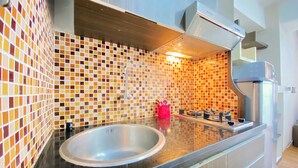 A modern kitchen with a black countertop, a stainless steel sink, a colorful mosaic backsplash, and a built-in range hood. - Homey 1Br At Jarrdin Cihampelas Apartment (Bandung)
