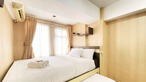 A neatly made bed with white linens and a rolled towel, a bedside table, and a wall-mounted air conditioning unit. - Homey 1Br At Jarrdin Cihampelas Apartment (Bandung)
