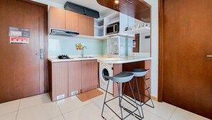 A compact kitchen with a washing machine, a microwave, and a sink. There are two stools under a counter. - Nice And Comfort 1Br Apartment At M-Town Signature (Gading Serpong)