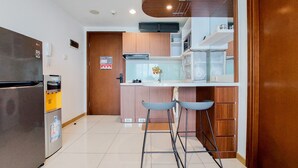 A modern kitchen with a built-in microwave, a stainless steel refrigerator, and a wooden cabinet. There are two blue bar stools and a white countertop. - Nice And Comfort 1Br Apartment At M-Town Signature (Gading Serpong)