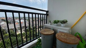 A balcony with a view of residential buildings, a radiator, potted plants, and two barrels. - Warm And Tidy Studio At Cinere Resort Apartment (Depok)