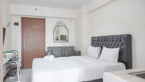 A hotel room with a large bed, a grey upholstered headboard, a white wall, and a wooden door. - Warm And Tidy Studio At Cinere Resort Apartment (Depok)