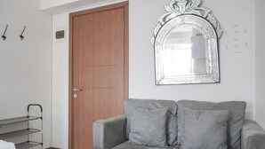 A room with a grey sofa, a wooden door, a metal shelf, and a decorative mirror. - Warm And Tidy Studio At Cinere Resort Apartment (Depok)