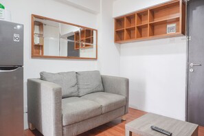 Un canapé gris avec des coussins, une table basse en bois, un miroir avec un cadre en bois, une étagère en bois et une porte grise.