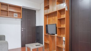 A room with a wooden TV stand, a small table with a remote, and a grey sofa. - Cozy And Tidy 1Br At Kebagusan City Apartment (Jakarta)