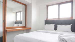 A neatly made bed with white linens and a rolled towel, a wooden nightstand, and a large mirror. - Cozy And Tidy 1Br At Kebagusan City Apartment (Jakarta)