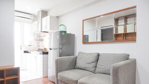 A modern living room with a grey sofa, a wooden coffee table, and a kitchen area with white cabinets and a grey refrigerator. - Cozy And Tidy 1Br At Kebagusan City Apartment (Jakarta)