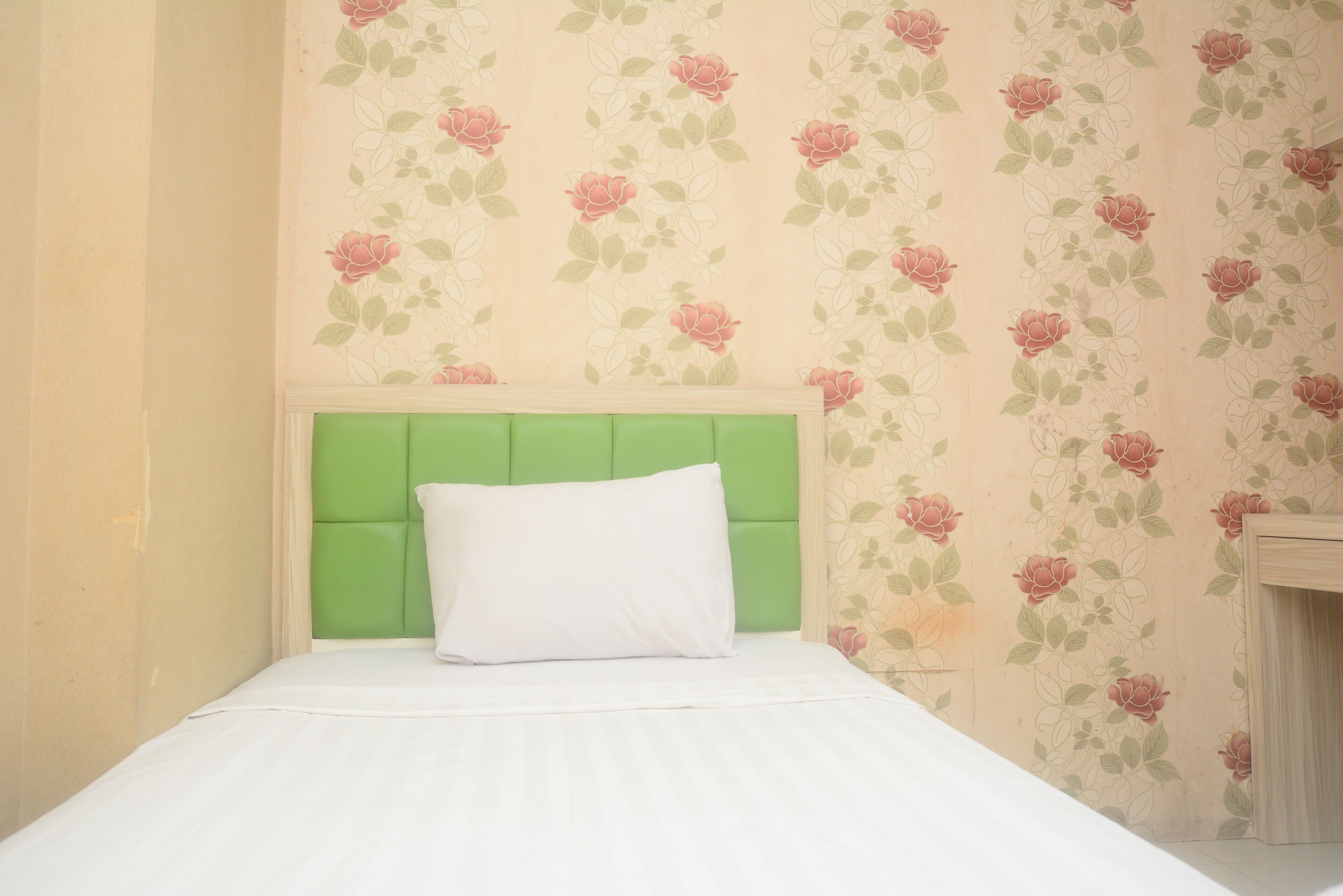 A bed with a green headboard and white bedding in a room with floral wallpaper.