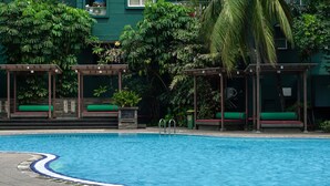 A swimming pool with a clear blue water, surrounded by green plants and a building with a green facade. - Spacious And Homey 2Br At Nuasa Hijau Pondok Indah Apartment (Jakarta)