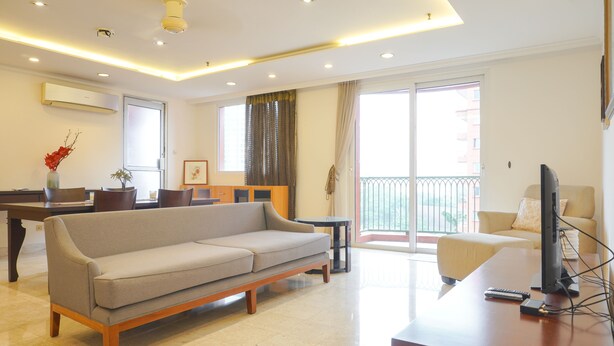 A modern living room with a sofa, a coffee table, and a flat-screen TV on a wooden desk. - Spacious And Homey 2Br At Nuasa Hijau Pondok Indah Apartment (Jakarta)