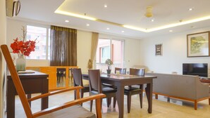 A modern living room with a dining area, a sofa, a TV, and a large window with curtains. - Spacious And Homey 2Br At Nuasa Hijau Pondok Indah Apartment (Jakarta)