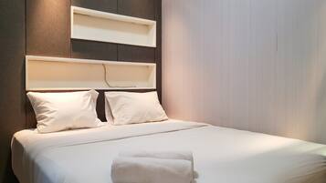 Un lit bien fait, avec du linge de lit blanc et des oreillers, une serviette blanche posée sur le lit, et une tête de lit dotée d’étagères intégrées.