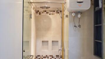 Une douche à l’italienne avec des parois en verre, une pomme de douche au plafond et une douchette à main, ainsi qu’un robinet mural.