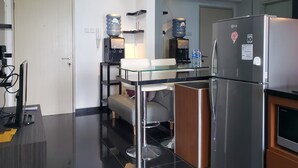 A modern kitchen with a stainless steel refrigerator, water dispensers, and a glass-top dining table. - Nice And Cozy Living 2Br Apartment At Green Bay Pluit (Jakarta)