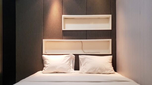 A bed with two pillows and a white headboard against a wooden wall. - Nice And Cozy Living 2Br Apartment At Green Bay Pluit (Jakarta)