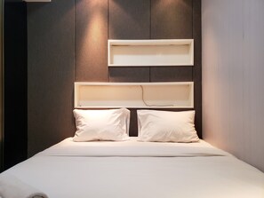 Cama com duas almofadas e cabeceira branca apoiada em parede de madeira.