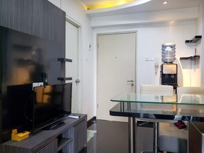 Uma sala de estar moderna com uma televisão de tela plana grande, uma mesa de jantar com tampo de vidro e um dispensador de água.