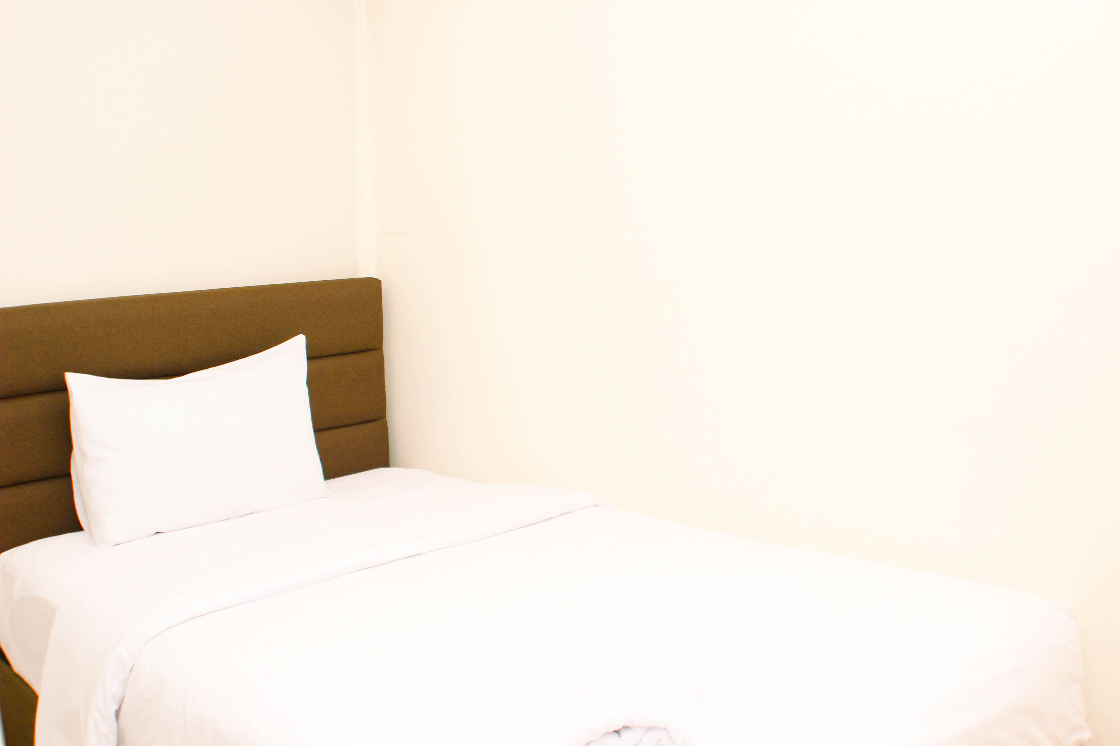Een bed met een bruin hoofdeinde en witte beddengoed.