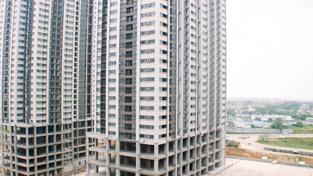 Un immeuble de grande hauteur, doté de nombreux étages et de balcons, entouré de chantiers et offrant une vue lointaine sur le paysage urbain.