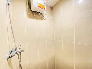 Ein Badezimmer mit beige fliesen Wänden, einer Dusche inklusive Handbrause und einem Warmwasserbereiter mit dem Aufdruck 'SAVEWAIT'.