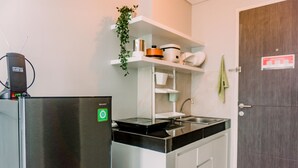 Una cucina compatta con piano cottura integrato, forno a microonde e frigorifero. Sopra il lavello, uno scaffale con diversi utensili da cucina.