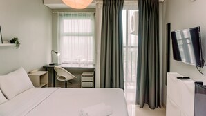 Una camera d'albergo con un letto, una scrivania, una sedia, televisione e tende.