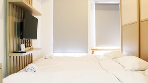 A hotel room with a bed, a TV on a wooden shelf, a closet, and a window with blinds. - Cozy Living Studio Apartment At High Floor Tokyo Riverside Pik 2 (Teluknaga)
