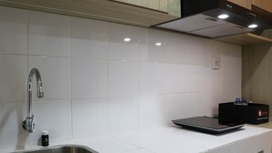 A modern kitchen with white tiles, a stainless steel sink, a black countertop, and a Rinnai range hood. - Cozy Living Studio Apartment At High Floor Tokyo Riverside Pik 2 (Teluknaga)