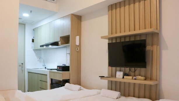 A hotel room with a bed, a TV mounted on the wall, a phone, and a small shelf with items. - Cozy Living Studio Apartment At High Floor Tokyo Riverside Pik 2 (Teluknaga)