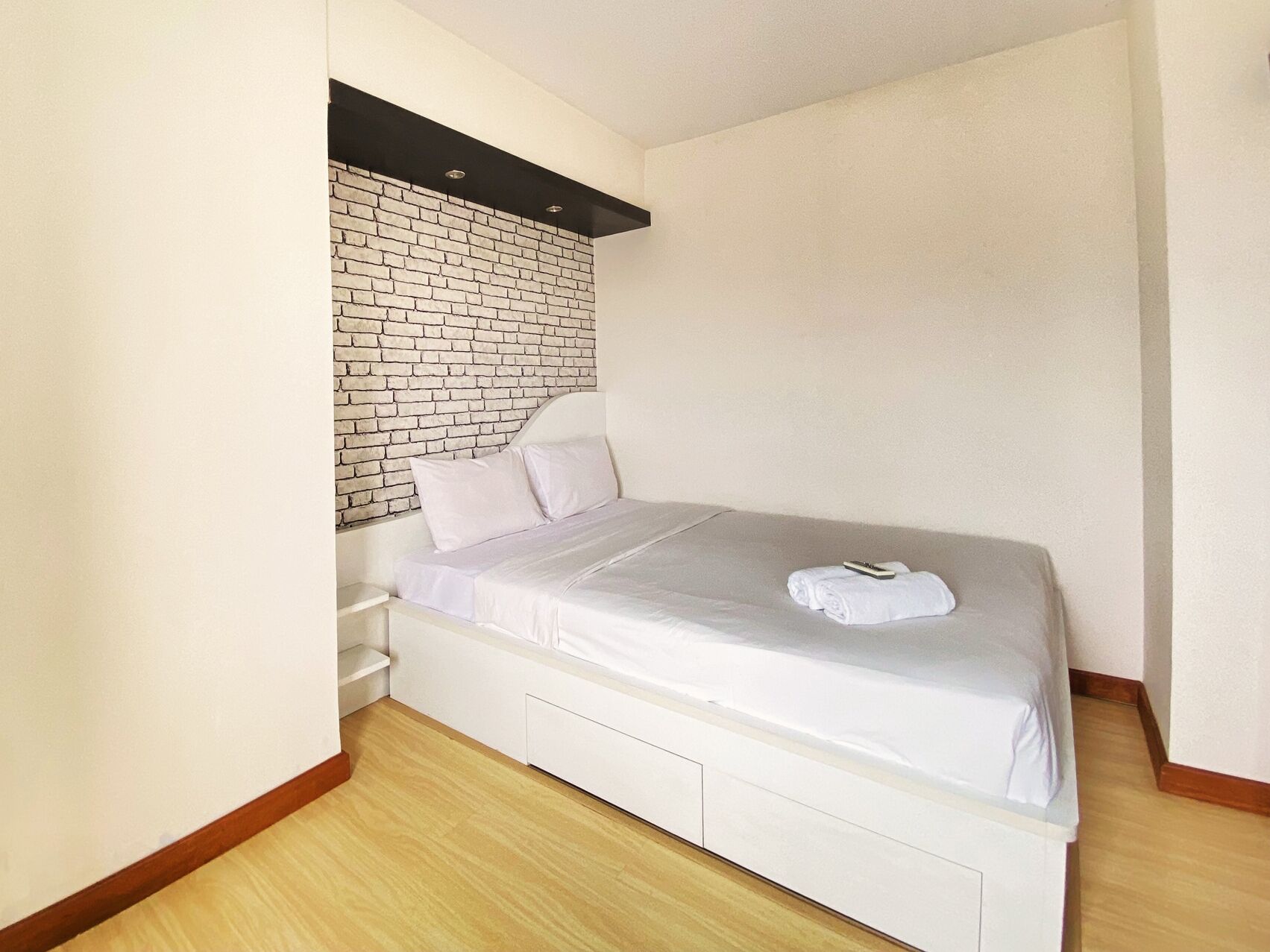A bedroom with a white bed, a brick accent wall, and a wooden floor.