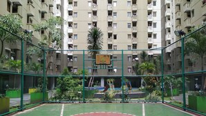 Un terrain de basket en plein air, entouré d’une clôture verte, avec un immeuble d’habitation en arrière-plan.