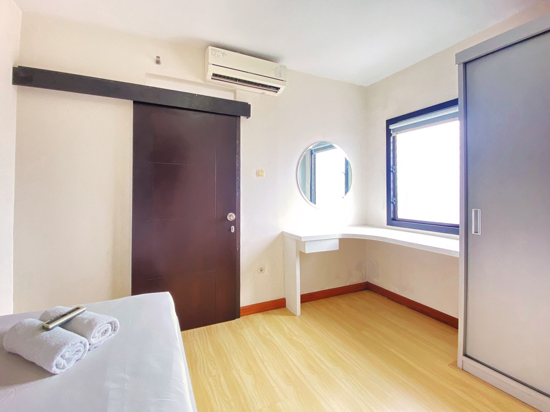 A hotel room with a bed, a desk, a window, and an air conditioning unit.