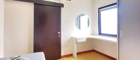 A hotel room with a bed, a desk, a window, and an air conditioning unit.