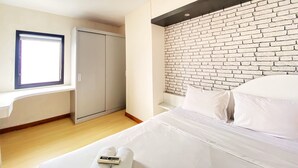 Une chambre à coucher avec un lit, une fenêtre, une armoire et un mur décoré d’un motif en briques.