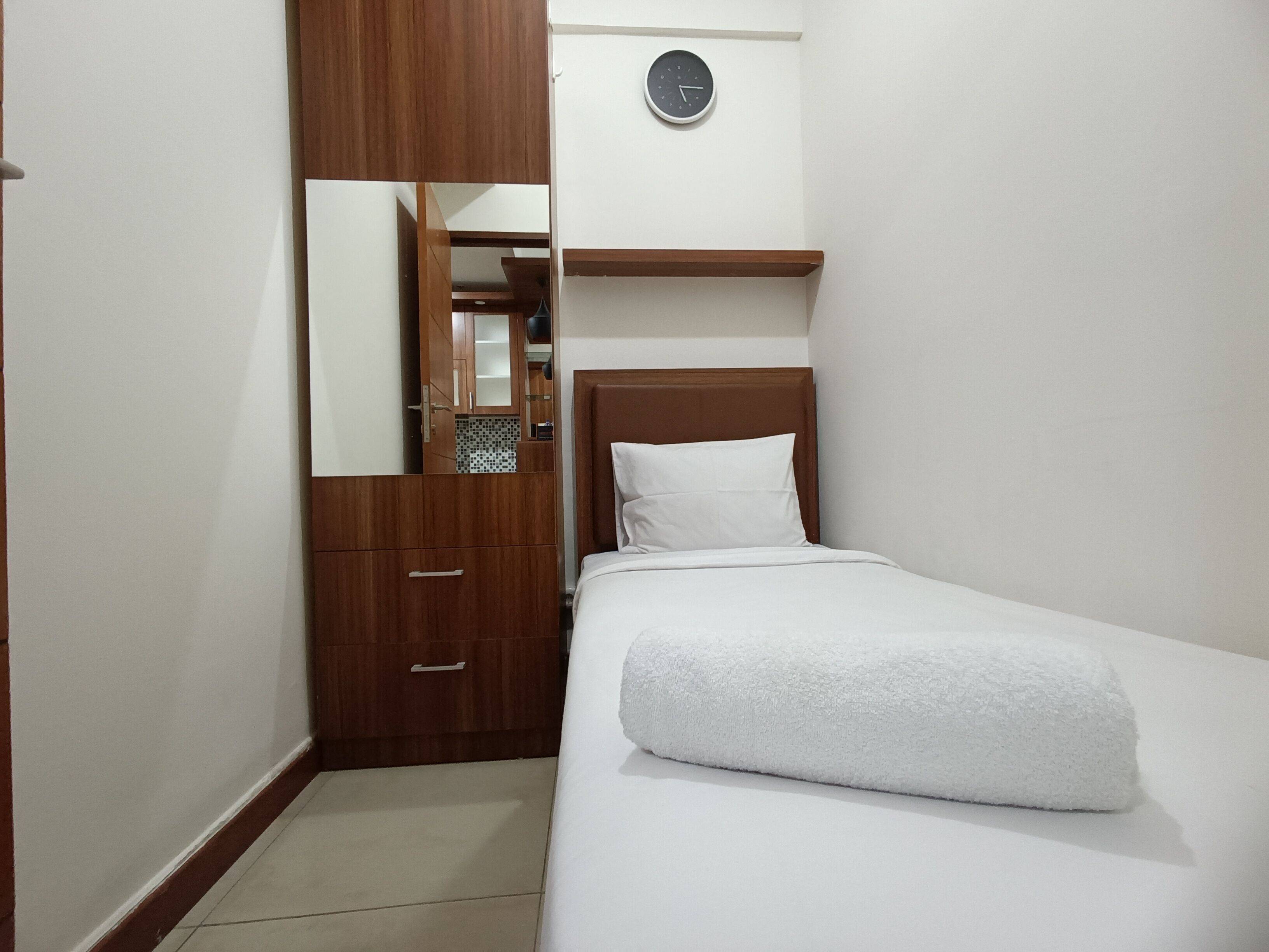 A bedroom with a bed, a wooden wardrobe, a mirror, and a clock on the wall.