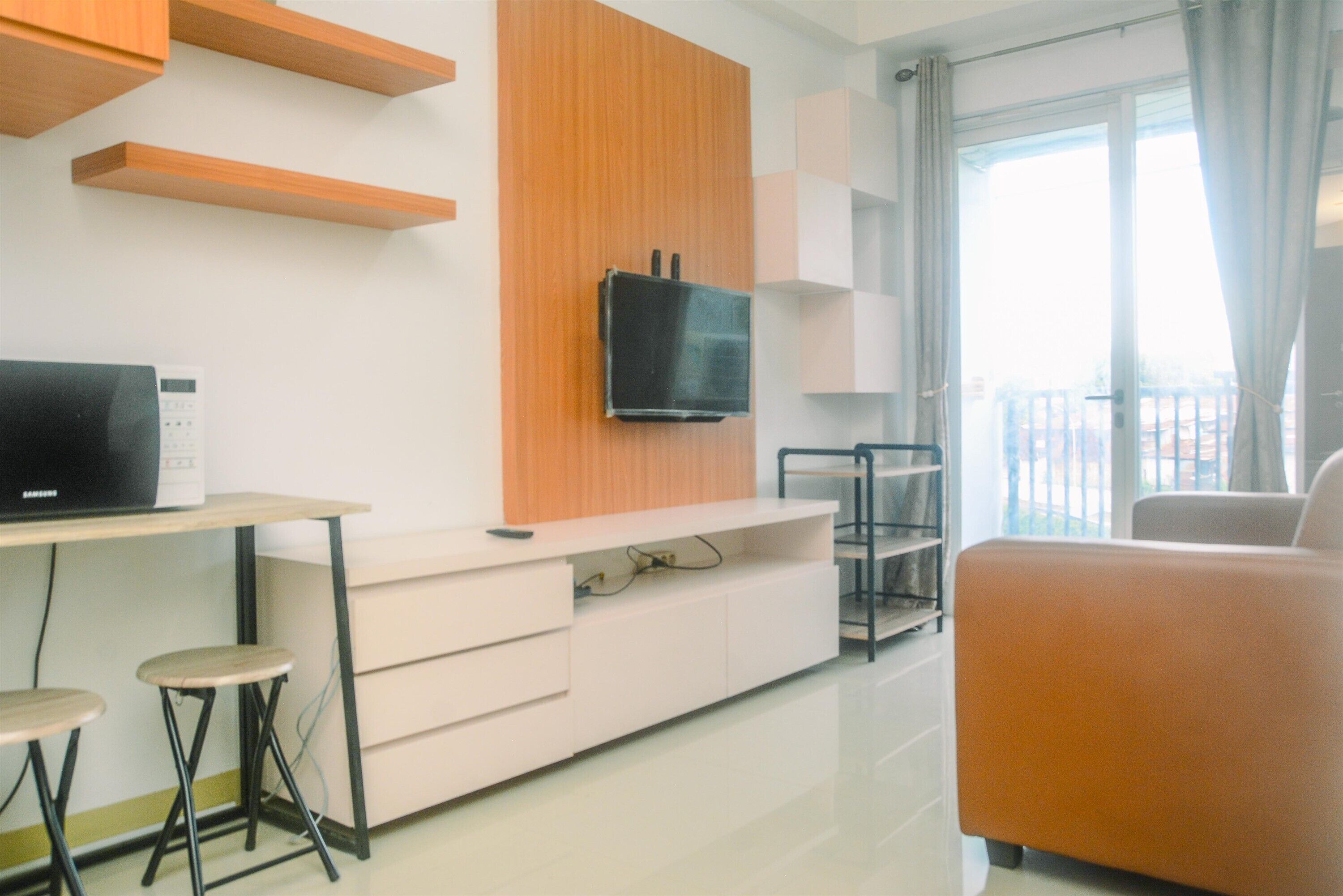 Uma sala de estar moderna com uma TV de tela plana fixada em um painel de madeira, um sofá branco e uma pequena mesa com banquinhos.
