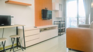 Una sala de estar moderna con una televisión de pantalla plana montada en un panel de madera, un sofá blanco y una pequeña mesa con taburetes.