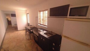 Eine kleine Küche mit Spüle, ein Essbereich mit Stühlen, ein Fenster mit Jalousien und ein Kühlschrank.