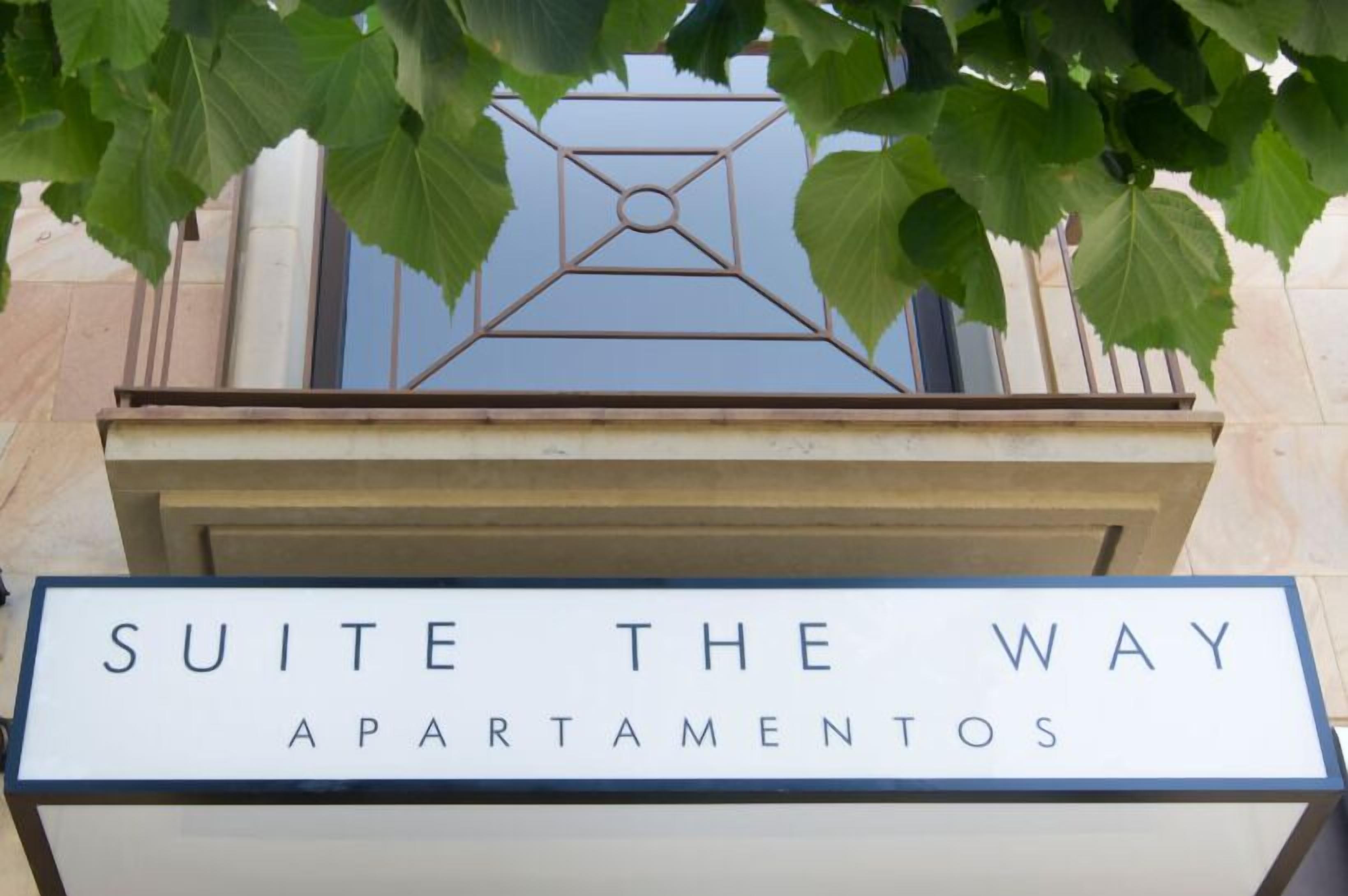 A sign for 'Suite The Way Apartamentos' with a geometric metal design above it.