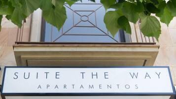 A sign for 'Suite The Way Apartamentos' with a geometric metal design above it.