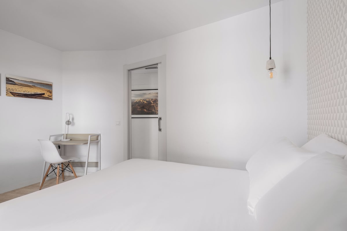 A minimalist bedroom with a bed, a desk, and a chair.