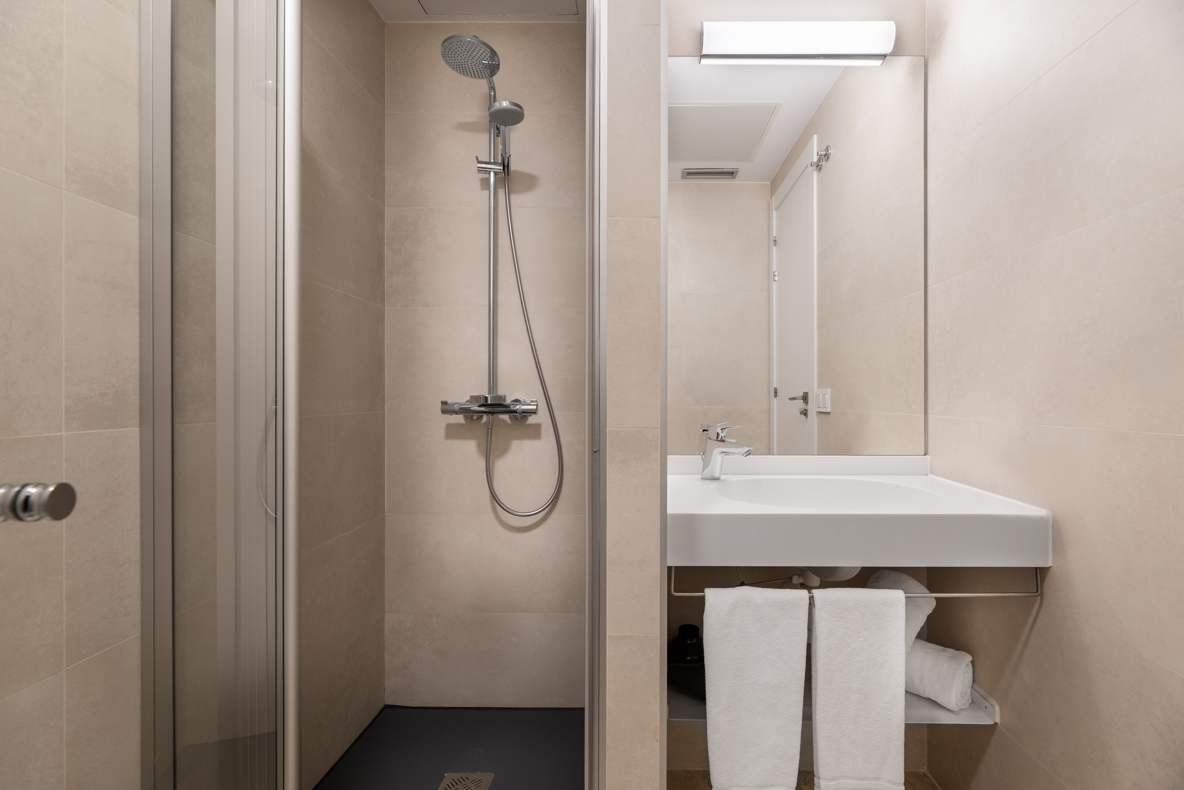 Un baño moderno con cabina de ducha de vidrio, un lavamanos blanco y un espejo sobre el lavamanos.